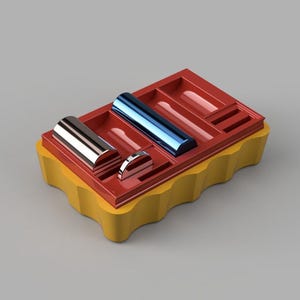 Puede incluir: Una caja de almacenamiento roja y amarilla con compartimentos para guardar objetos pequeños. La caja tiene un borde ondulado y contiene dos objetos cilíndricos plateados y azules y dos discos plateados.