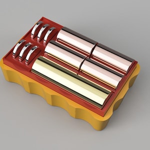 Puede incluir: Un soporte de baterías amarillo y rojo con cuatro baterías cilíndricas. Las baterías son doradas, de cobre y plateadas.