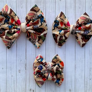 May include: Three different sizes of hair bows with a cream background and a colorful print of characters from the movie "Zootopia".