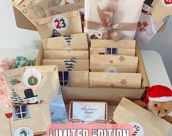 May include: A cardboard box filled with twenty-four numbered paper envelopes featuring Christmas illustrations like snowmen, trees, and ornaments. A gift-wrapped package with a ribbon and a business card for Moondreamer Studio are included.
