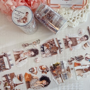 以下が含まれることがあります： カフェのイラストが描かれた装飾用マスキングテープとステッカー。1つのロールには「Brew & Browse by Moondreamer Studio」と書かれています。ステッカーは、人々、コーヒー、カフェの要素を描いています。