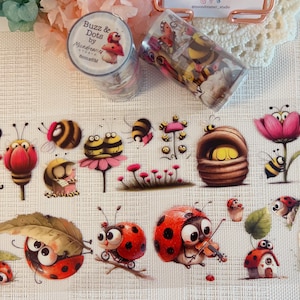 Op de afbeelding: Twee rollen decoratieve washi-tape met cartoonbijen en lieveheersbeestjes. Eén rol is gelabeld met Buzz & Dots by Moondreamer Studio 8cmx6M. Het ontwerp toont diverse illustraties van insecten, bloemen en paddenstoelen in levendige kleuren.