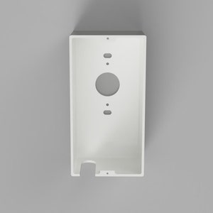 May include: A rectangular white mounting bracket for a smart doorbell, featuring a large central circular cutout, two smaller oval openings, and several screw holes, with a notched opening at the bottom edge for cable routing.