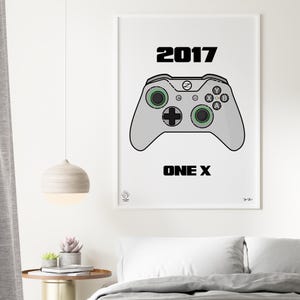 May include: A white framed poster with a black and white illustration of a video game controller. The text "2017 ONE X" is printed below the controller.