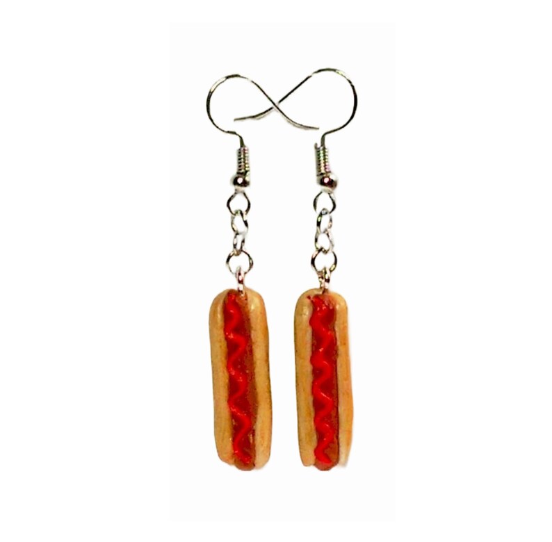 May include: A pair of silver dangle earrings with a miniature hot dog charm. The hot dog is made of polymer clay and has a red ketchup topping.