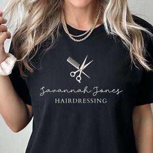 Puede incluir: Camiseta negra con un gráfico blanco de tijeras y un peine, y el texto "Savannah Jones Hairdressing".
