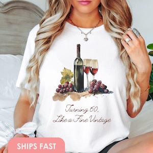 Pode incluir: Camiseta branca com uma ilustra&ccedil;&atilde;o em aquarela de uma garrafa de vinho e duas ta&ccedil;as de vinho. O texto "Turning 60, Like a Fine Vintage" est&aacute; impresso na camiseta.