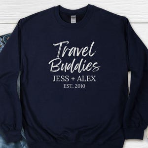 May include: Navy blue long-sleeved sweatshirt with white text that reads "Travel Buddies Jess + Alex Est. 2010".