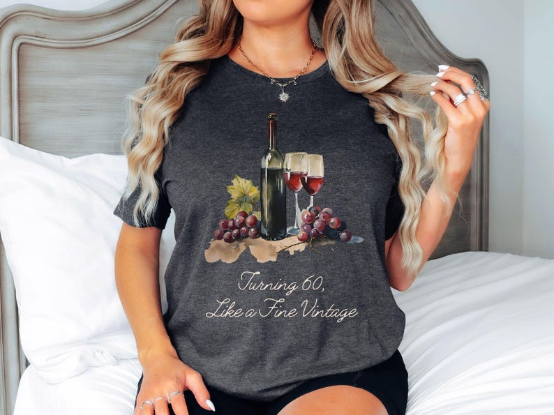Pode incluir: Uma camiseta cinza escura com um gr&aacute;fico de uma garrafa de vinho e duas ta&ccedil;as de vinho. O texto "Turning 60, Like a Fine Vintage" est&aacute; impresso na camiseta.