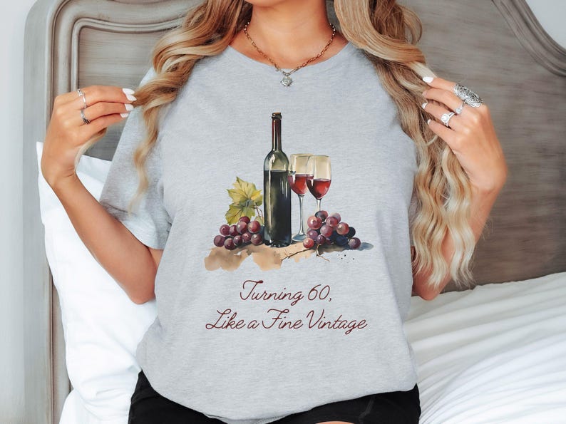 Pode incluir: Camiseta cinza com uma ilustra&ccedil;&atilde;o em aquarela de uma garrafa de vinho, duas ta&ccedil;as de vinho e uvas. O texto "Turning 60, Like a Fine Vintage" est&aacute; impresso na camiseta.
