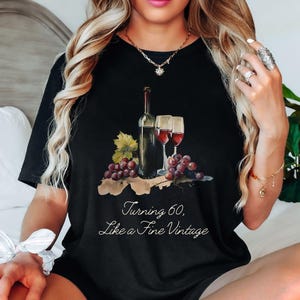 Pode incluir: Camiseta preta com um gr&aacute;fico de uma garrafa de vinho e duas ta&ccedil;as de vinho. O texto "Turning 60, Like a Fine Vintage" est&aacute; impresso na camiseta.