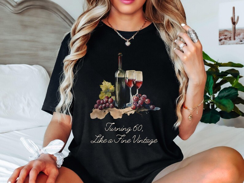 Pode incluir: Camiseta preta com um gr&aacute;fico de uma garrafa de vinho e duas ta&ccedil;as de vinho. O texto "Turning 60, Like a Fine Vintage" est&aacute; impresso na camiseta.