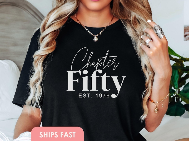 May include: Black t-shirt with the words "Chapter Fifty" in white script and block letters, with "EST. 1976" below. The shirt is a casual style, suitable for milestone birthdays. The image shows the shirt on a person.