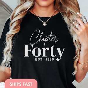 Może przedstawiać: Czarny t-shirt z napisem "Chapter Forty" w ozdobnej czcionce nad słowem "Forty" pogrubioną czcionką. Tekst "EST. 1986" znajduje się poniżej. Odzież z motywem urodzinowym, idealna na 40. urodziny.