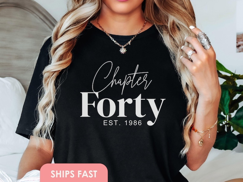 Może przedstawiać: Czarny t-shirt z napisem "Chapter Forty" w ozdobnej czcionce nad słowem "Forty" pogrubioną czcionką. Tekst "EST. 1986" znajduje się poniżej. Odzież z motywem urodzinowym, idealna na 40. urodziny.