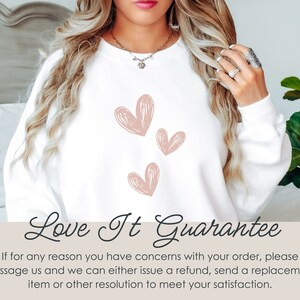 May include: White sweatshirt with a pink heart design and the text "Love It Guarantee". The text below the design reads "If for any reason you have concerns with your order, please message us and we can either issue a refund, send a replacement item or other resolution to meet your satisfaction."