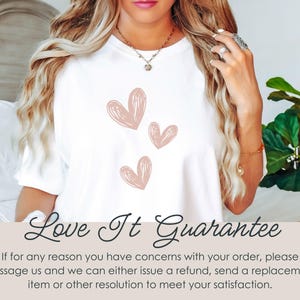 May include: White t-shirt featuring three pink heart designs. The text "Love It Guarantee" is displayed at the bottom of the image.