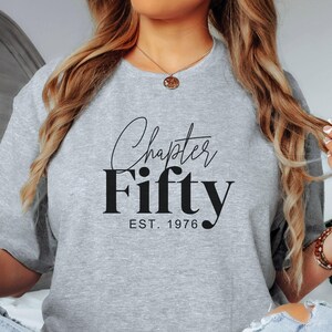 May include: A light gray sweatshirt with the words "Chapter Fifty" in a black script font, with "EST. 1976" below. The sweatshirt is a crew neck style.