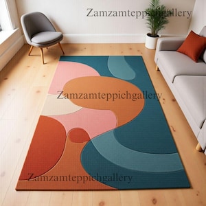 May include: A rectangular area rug with an abstract design. The rug features a teal background with large, overlapping shapes in shades of orange, pink, and light blue. The rug is placed on a hardwood floor, with a gray chair and sofa visible.
