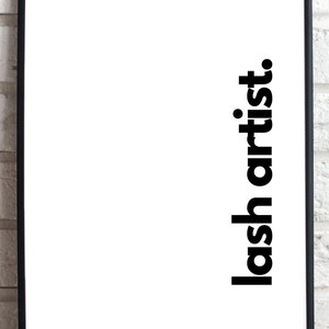 May include: A black framed print with the text "lash artist." printed vertically in bold, black font on a white background.