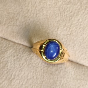 May include: A gold ring with a blue star sapphire gemstone. The ring has a simple band with a raised setting for the stone.