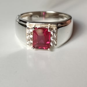 May include: A silver ring with a large, square, red gemstone surrounded by smaller, white gemstones.