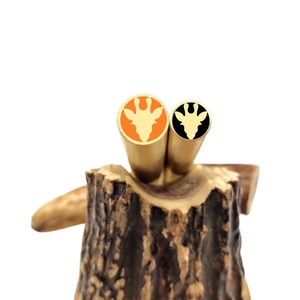 May include: Two brass pen blanks with a giraffe head design. The blanks are in a wooden holder. One blank is orange with a gold giraffe head, and the other is black with a gold giraffe head.