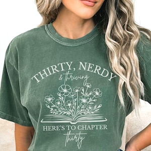 May include: A green t-shirt with a white graphic design that says "Thirty, Nerdy & Thriving. Here's to Chapter Thirty." The graphic features a book with flowers growing out of it.