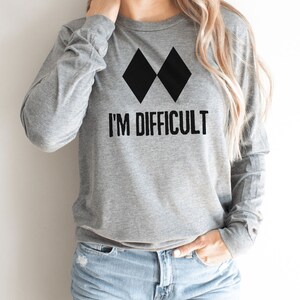 May include: Gray long-sleeve shirt with black double diamond symbol and the text "I'M DIFFICULT".