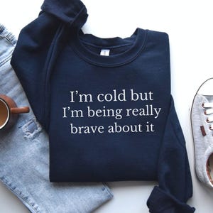 May include: A navy blue sweatshirt with the text "I'm cold but I'm being really brave about it" in white.