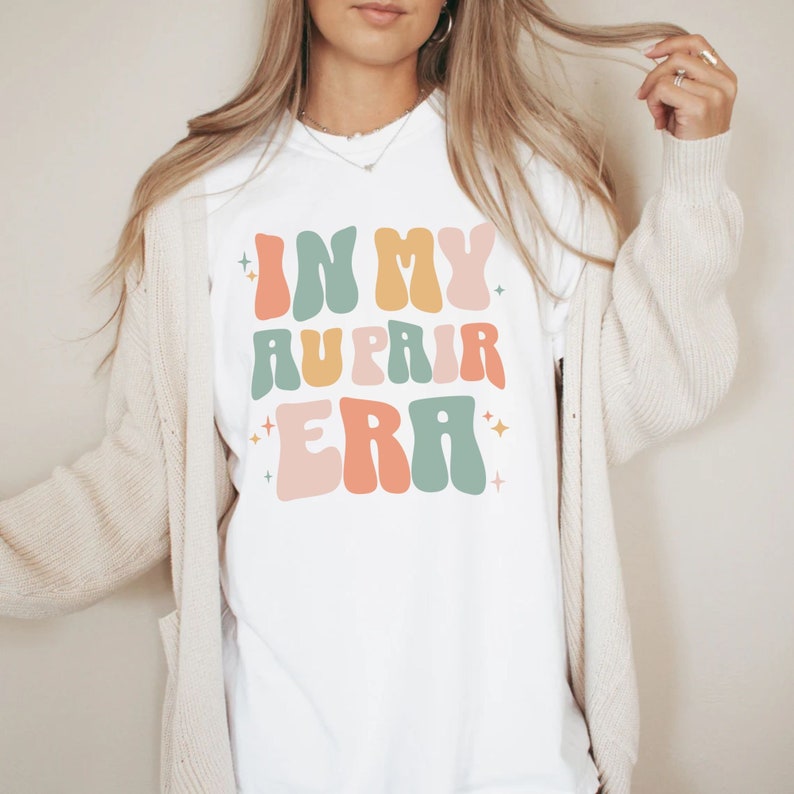 May include: White t-shirt with the text "In My Au Pair Era" in colourful retro font.