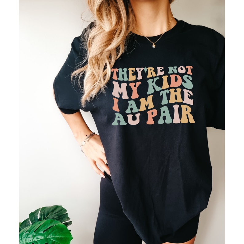 Pode incluir: Camiseta preta com um gr&aacute;fico colorido que diz "They're not my kids I am the au pair".