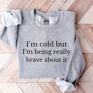 May include: Gray sweatshirt with the text "I'm cold but I'm being really brave about it" printed on the front.