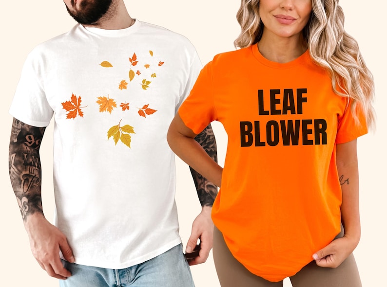 May include: Two short-sleeved t-shirts. One is white with orange and yellow autumn leaves. The other is orange with the words "LEAF BLOWER" in black block letters. The shirts are casual wear.