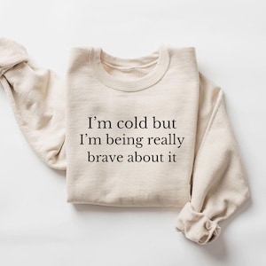 May include: A beige sweatshirt with the text "I'm cold but I'm being really brave about it" printed on the front.