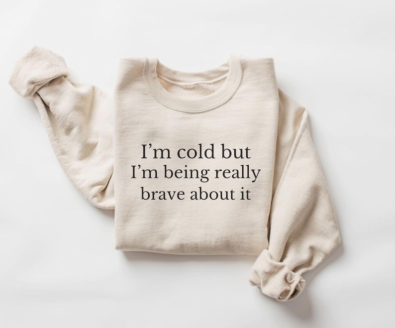May include: A beige sweatshirt with the text "I'm cold but I'm being really brave about it" printed on the front.