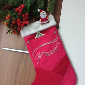 May include: A red and white Christmas stocking with a denim pocket and silver embellishments. The stocking has a white faux fur cuff and a small Santa figurine on top.