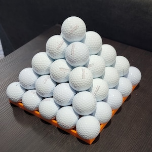 May include: A pyramid of white golf balls with the Kirkland Signature logo on each ball. The balls are arranged on a small orange tray.