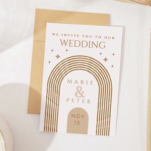 May include: A white wedding invitation with a brown and tan rainbow arch design. The text reads "We invite you to our wedding, Marie & Peter, Nov 15".