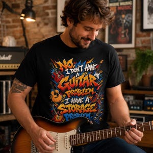 May include: A black short-sleeve t-shirt featuring a colorful graphic print with various electric and acoustic guitars. The text reads: NO, I DON'T HAVE A GUITAR PROBLEM. I HAVE A STORAGE PROBLEM. The design uses bold, stylized lettering and vibrant colors.