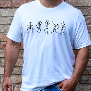 May include: White t-shirt with a graphic of five skeletons dancing. The skeletons are black and white and are in different poses.