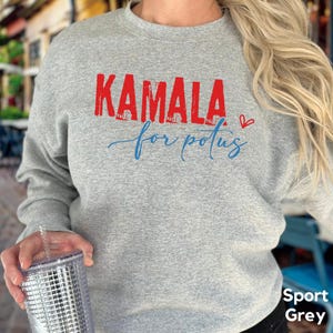 May include: A gray sweatshirt with the text "KAMALA for POTUS" in red and blue lettering. A small red heart is next to the text. The sweatshirt is a sport grey color.
