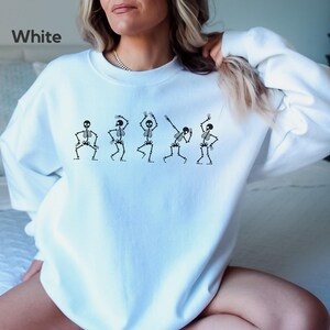 May include: White sweatshirt with a graphic of five skeletons dancing. The text "White" is in the top left corner of the image.