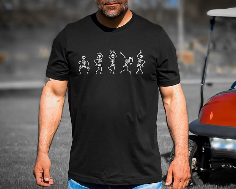 May include: A black t-shirt with a white graphic of five skeletons dancing. The skeletons are in various poses, with their arms and legs outstretched.