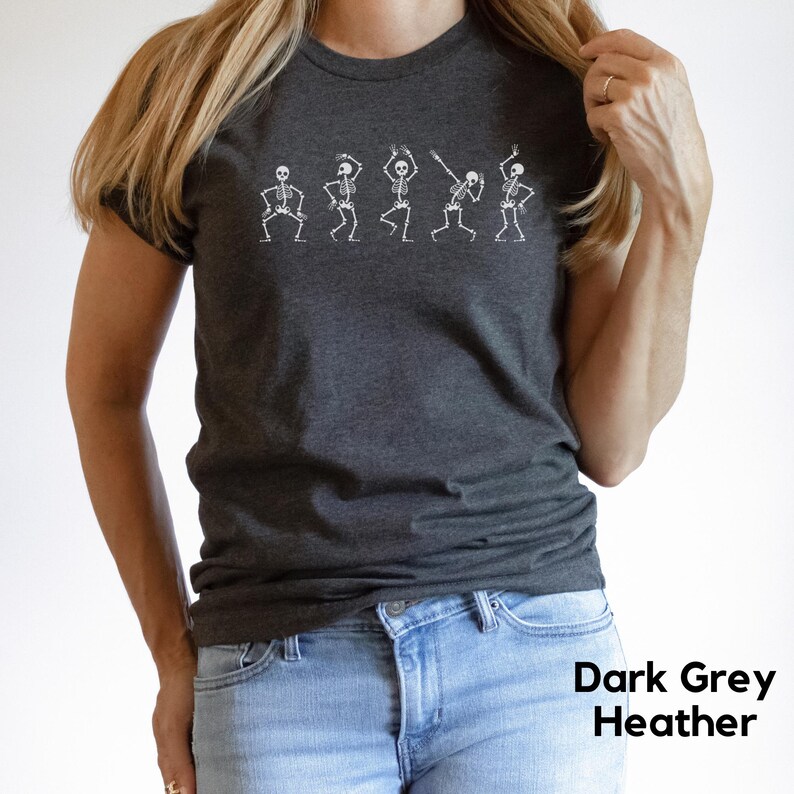 May include: A dark grey heather t-shirt featuring a line of five skeletons dancing. The skeletons are white and outlined in black.