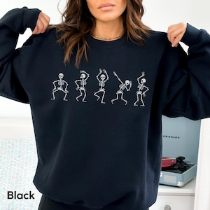 May include: Black sweatshirt with a graphic of five skeletons dancing. The skeletons are white and outlined in black.