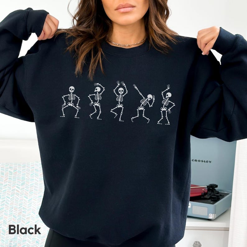 May include: Black sweatshirt with a graphic of five skeletons dancing. The skeletons are white and outlined in black.