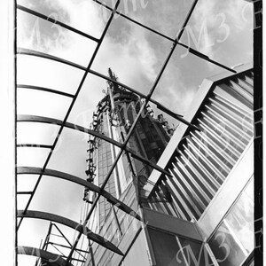 May include: Black and white photo of a skyscraper viewed from below, looking up at the top of the building. The building is made of glass and steel, and the photo is taken from a perspective that makes the building look very tall.