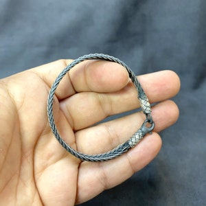 May include: A silver braided bracelet with a clasp closure. The bracelet is made of two different shades of silver, creating a unique and stylish look.