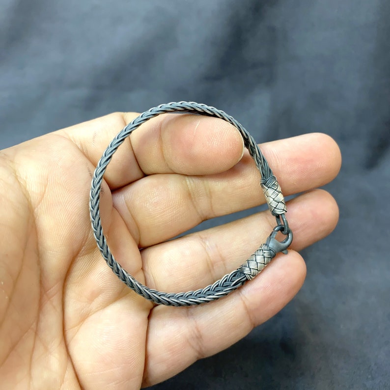 May include: A silver braided bracelet with a clasp closure. The bracelet is made of two different shades of silver, creating a unique and stylish look.